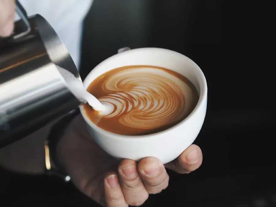 Lattiera che versa latte nel cappuccino per una schiuma perfetta