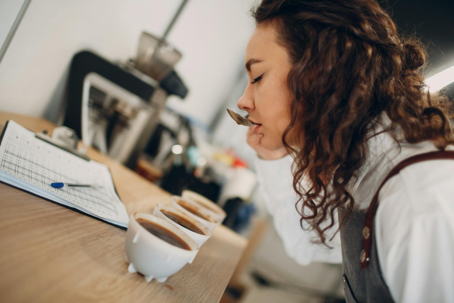 Assaggiatrice di caffè gusta differenti tipi dalle tazzine con un cucchiaio