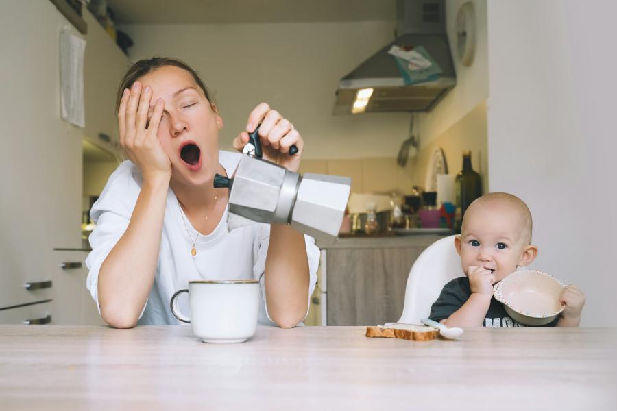 Mamma e bambino seduti al tavolo, la mamma sbadiglia stanca versando il caffè nella tazza dalla moka.