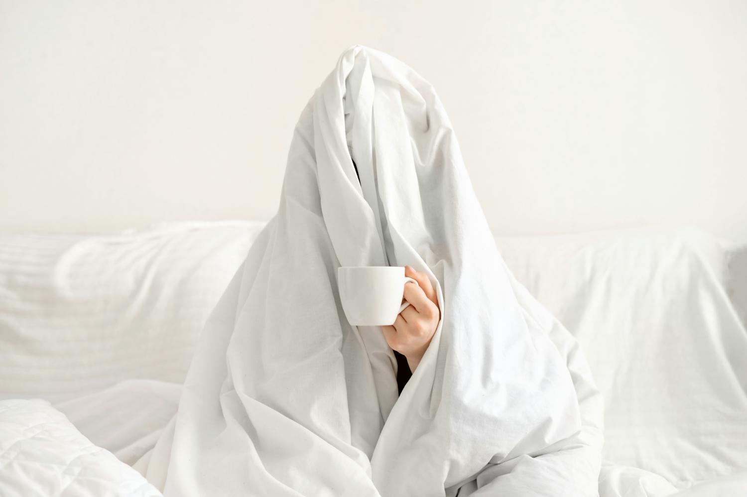Persona avvolta in una coperta bianca con una tazza di caffè in mano