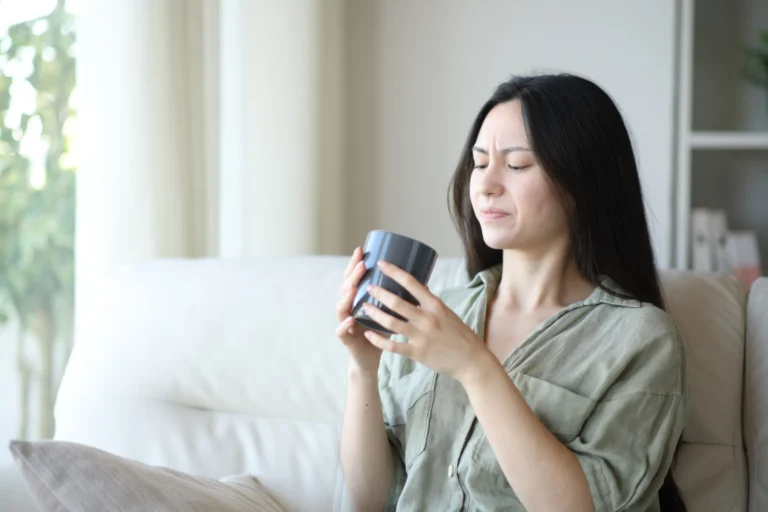 Ragazza che beve un caffè seduta sul divano con la faccia contraddetta come se il caffè fosse scaduto