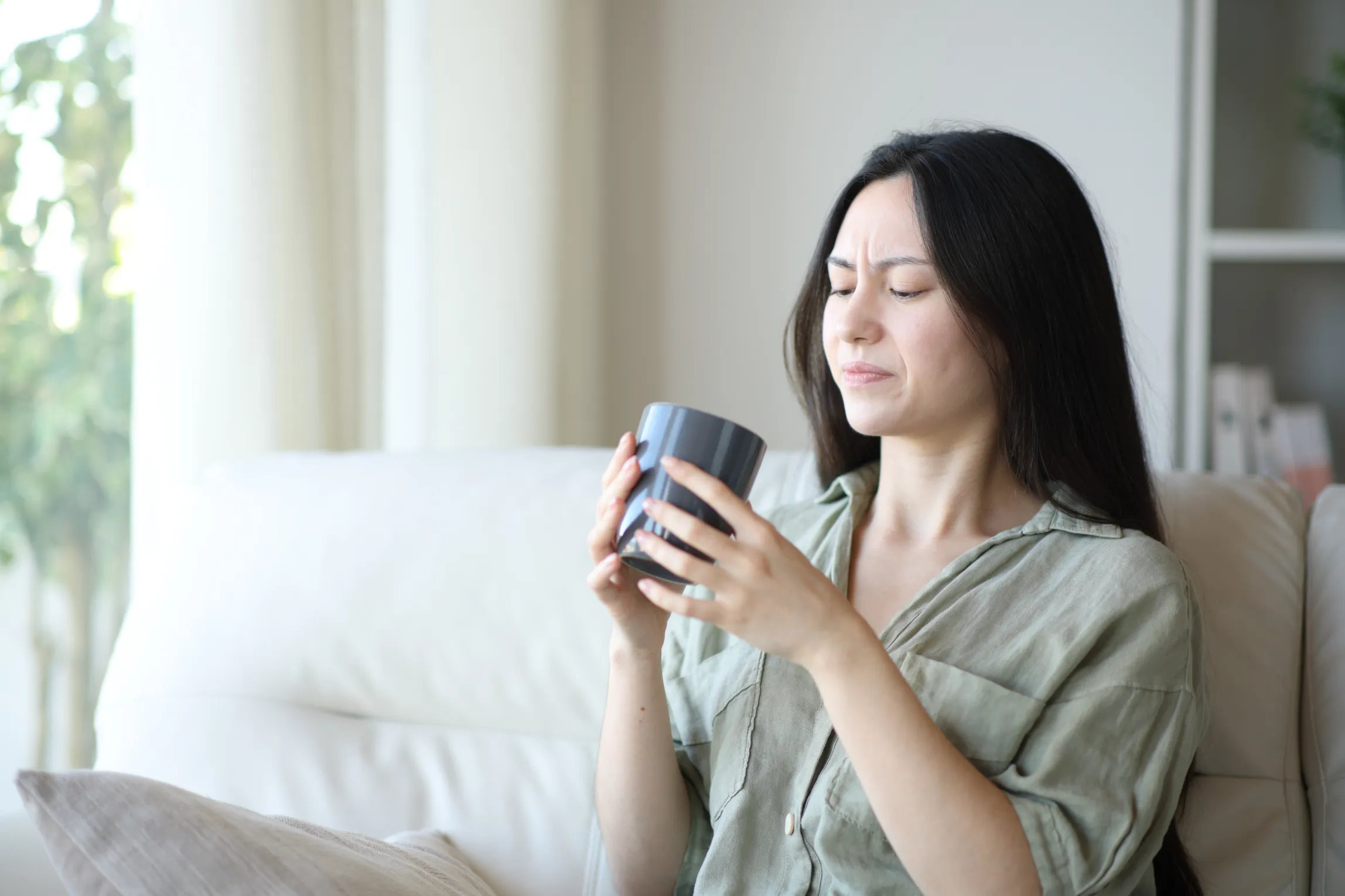 Ragazza che beve un caffè seduta sul divano con la faccia contraddetta come se il caffè fosse scaduto