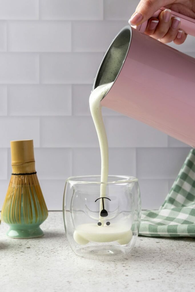 Tazza in vetro con latte che viene versato da un cappuccinatore
